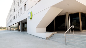 Una entrada de hotel moderna con fachada geométrica, una escalera y una puerta de vidrio que da al interior.