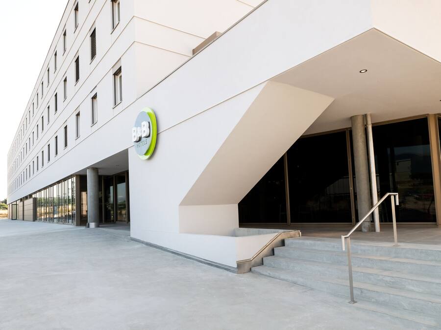 A modern hotel entrance with a geometric facade, a staircase, and a glass door leading inside.