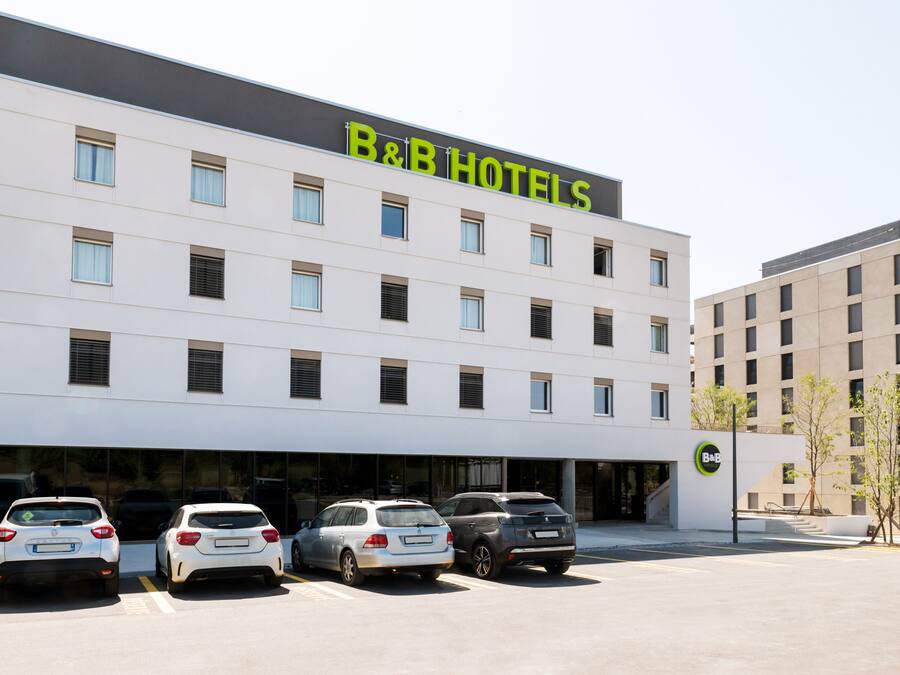 A B&B hotel with a modern facade, multiple floors, and a parking lot with several cars.
