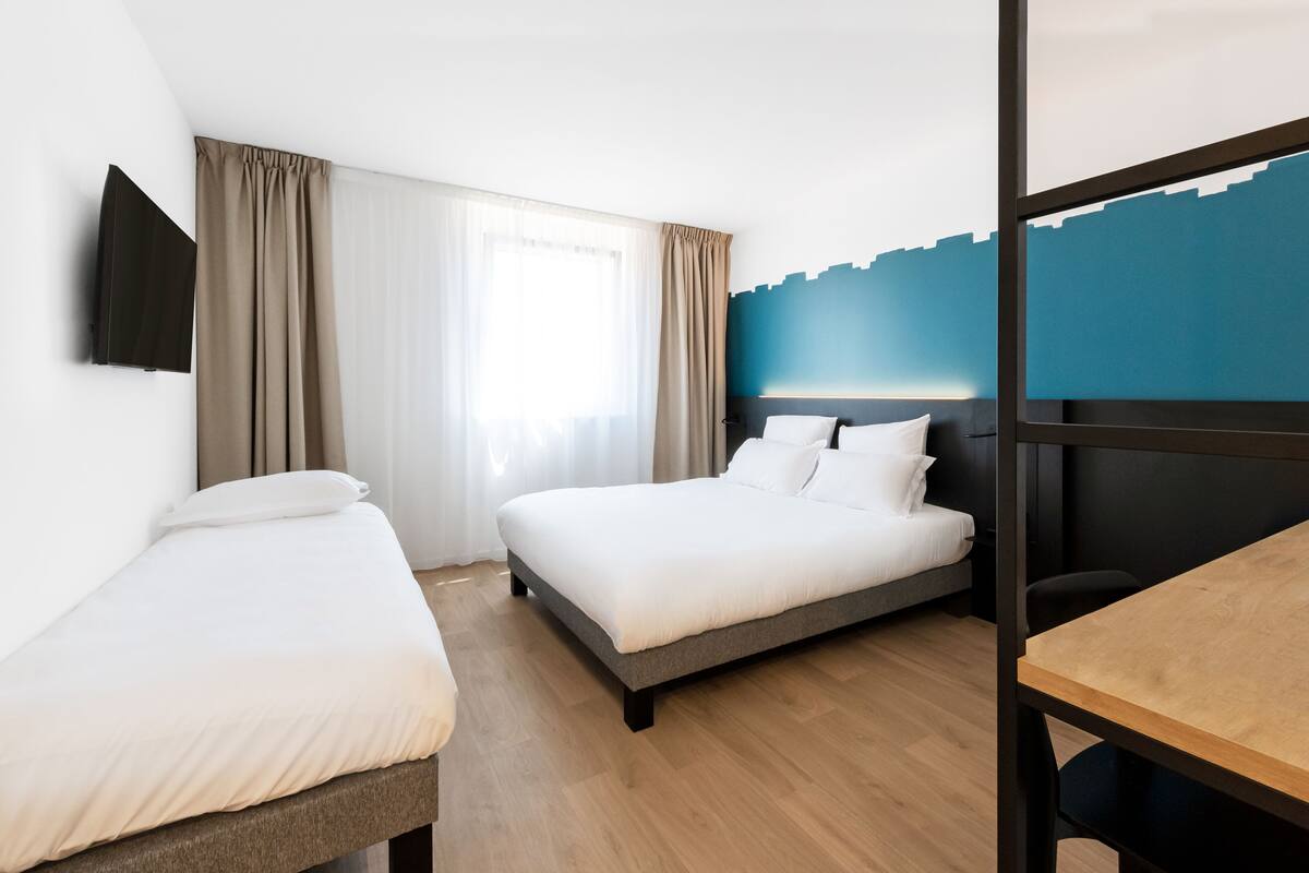 A hotel room with a bed, a desk, and a TV mounted on the wall.