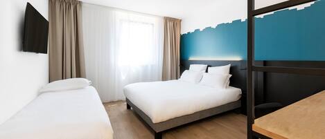 A hotel room with a bed, a desk, and a TV mounted on the wall.