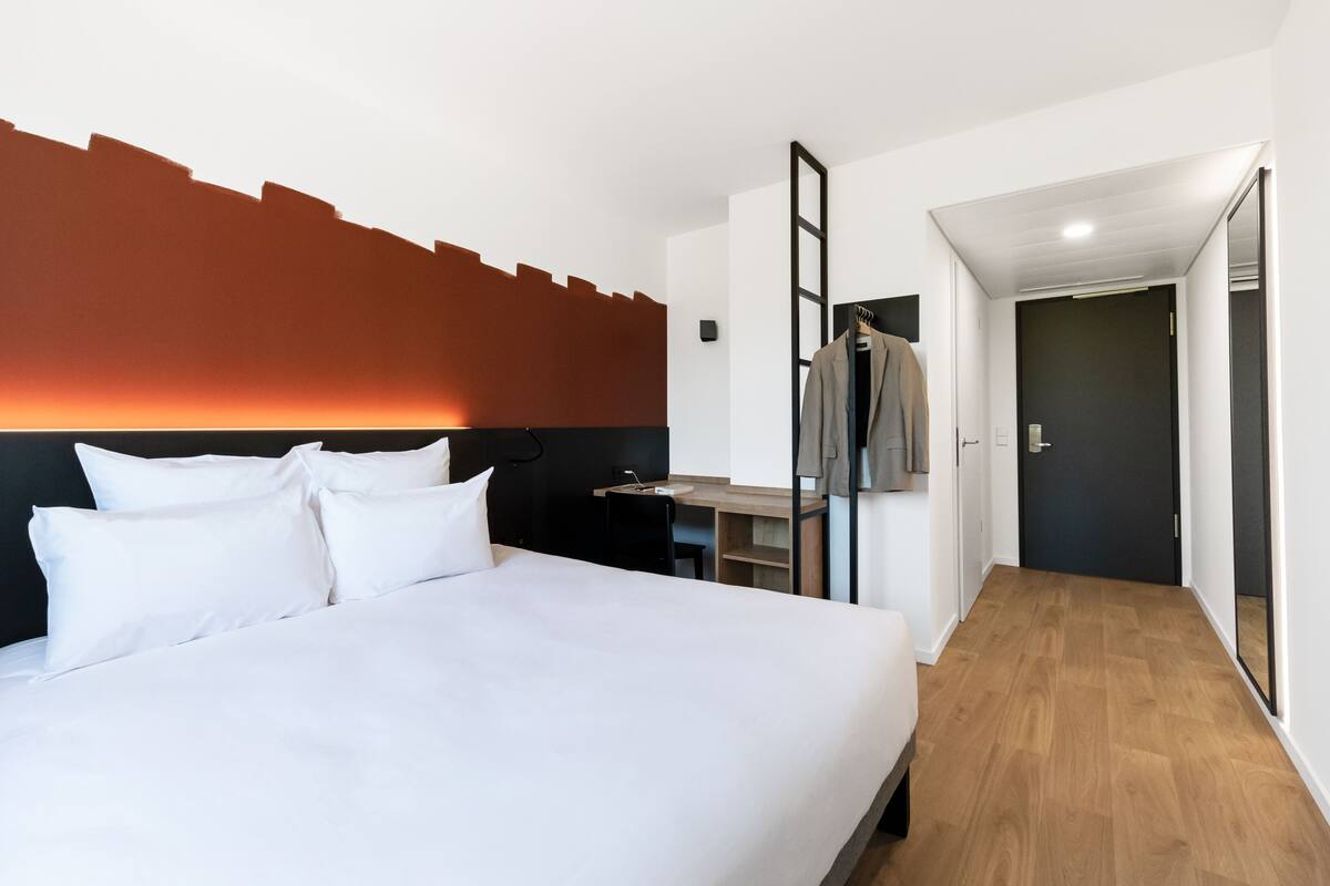 A hotel room with a large bed, a desk, and a wardrobe.