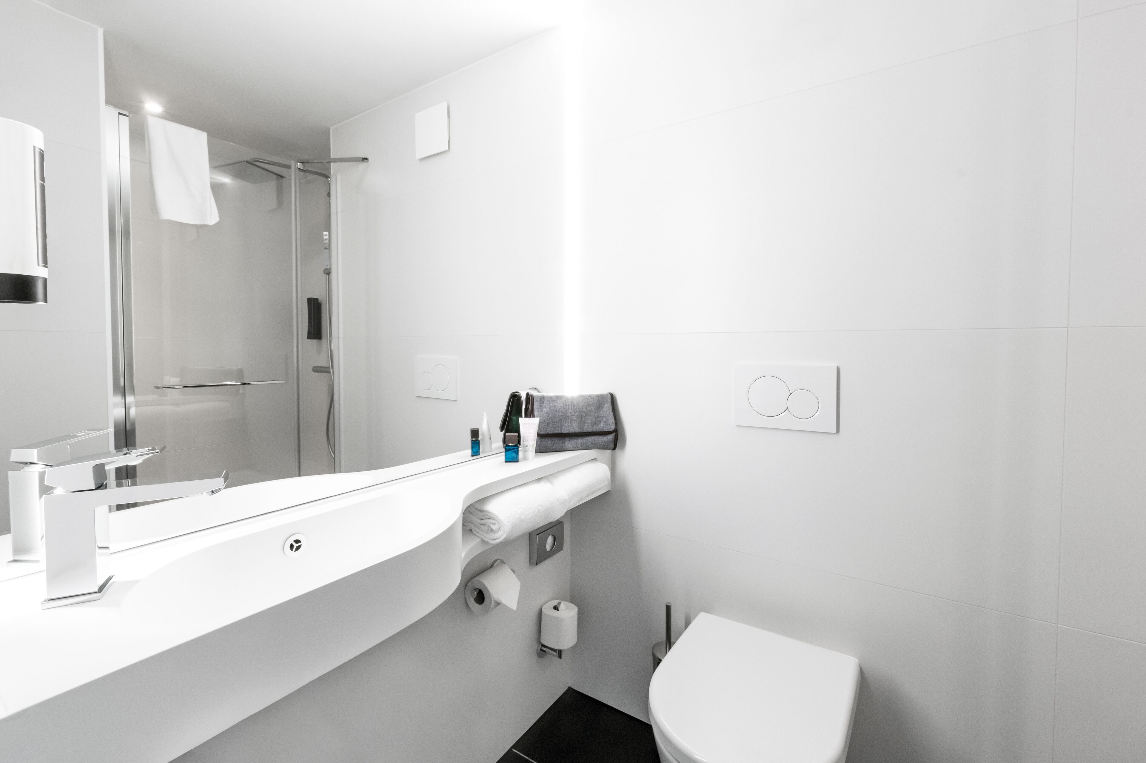 A modern bathroom with a white sink, mirror, and toilet. There is a towel rack with a towel and a bottle of soap.