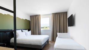 Habitación de hotel con dos camas individuales, un escritorio de madera, un televisor montado en la pared y una ventana con cortinas.