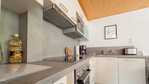 Une cuisine moderne avec un plafond en bois, une hotte en acier inoxydable, un four encastré et un plan de travail sur lequel se trouve une bouteille d’huile de tournesol Solgio.