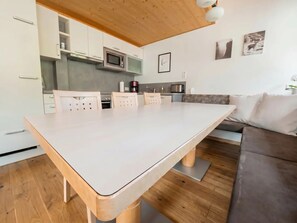 A modern kitchen with white cabinets, a large island, and a dining area with a wooden table and chairs.