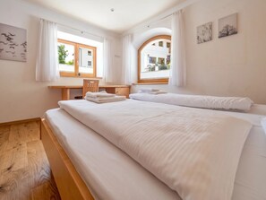 A hotel room with a large bed, a wooden desk, and two windows.