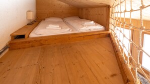 Une pièce en bois avec un lit, une table de chevet et un filet en corde tendu devant la fenêtre.