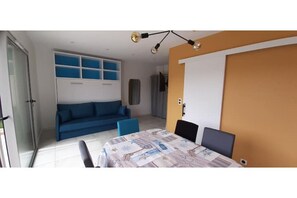 A room with a dining table, chairs, a sofa, and a TV.