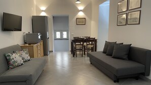 Una sala moderna con un sofá gris, televisor y comedor con mesa y sillas.