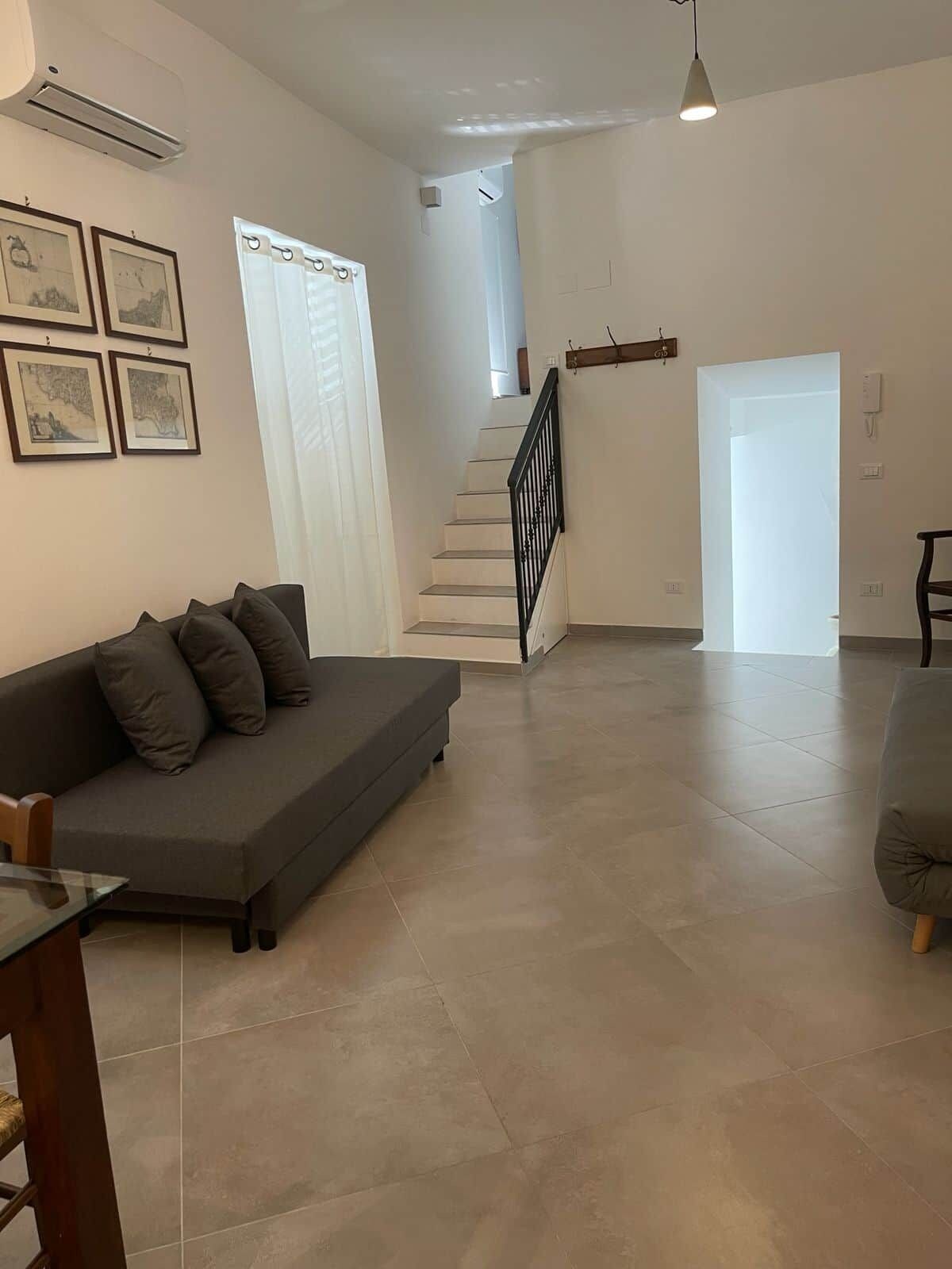 A spacious living area with a gray sofa, a dining table, and a staircase leading to another room.