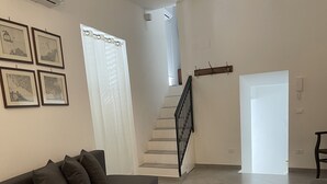 Un amplio salón con un sofá gris, una escalera y una puerta que da a otra habitación.