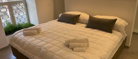A large bed with a quilted white duvet, two pillows, and a bedside table with a lamp.