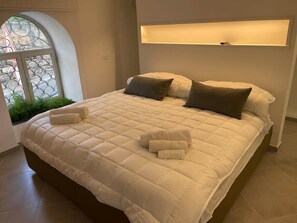 A large bed with a quilted white duvet, two pillows, and a bedside table with a lamp. - Cathedral House Design (Palermo)