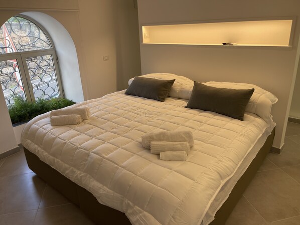A large bed with a quilted white duvet, two pillows, and two folded towels. - Cathedral House Design (Palermo)