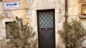 Un edificio con una puerta negra, dos macetas con plantas y un letrero que indica una panadería que ofrece comida siciliana.