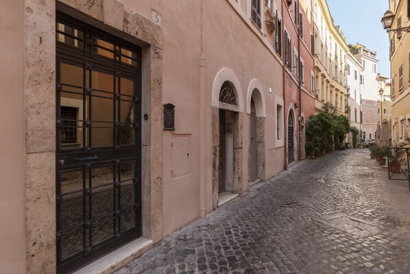 A narrow cobblestone street lined with historic buildings, featuring a large metal gate and arched windows. - GuestHost - Heart of Trastevere Mini APT (Rome)