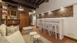 Una sala de estar acogedora con chimenea, estantería, sofá y un comedor con taburetes.
