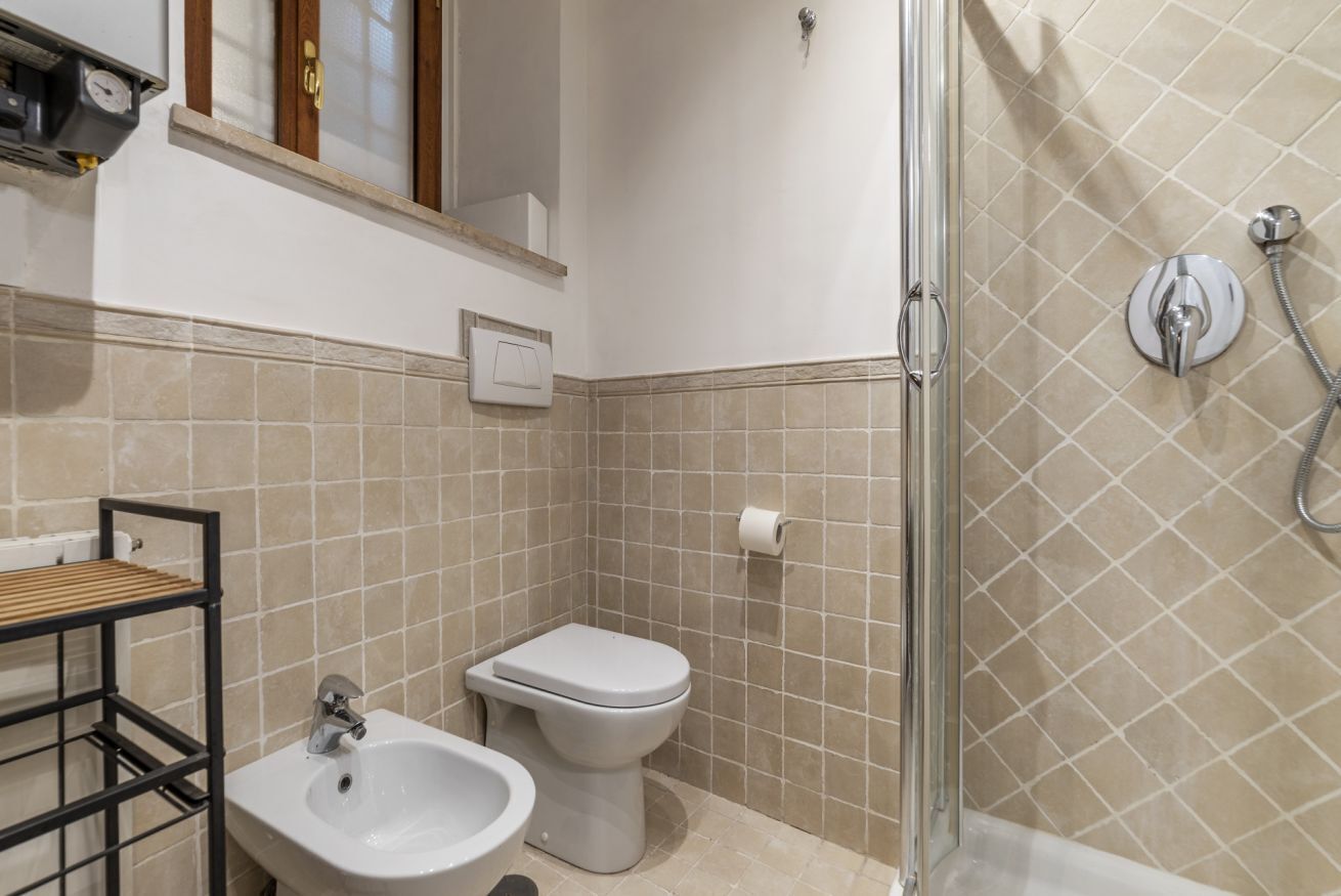 A bathroom with a shower, toilet, sink, and a shelf with a mirror.