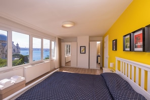 Ett hotellrum med en stor säng, utsikt över havet och en ljusgul vägg.