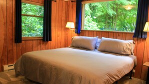 Un dormitorio con una cama grande, paredes de madera y ventanas con cortinas.