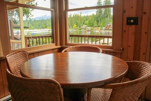 Enjoy meals in this cozy dining area with a round table and wicker chairs, surrounded by large windows offering a view of the lake and mountains.