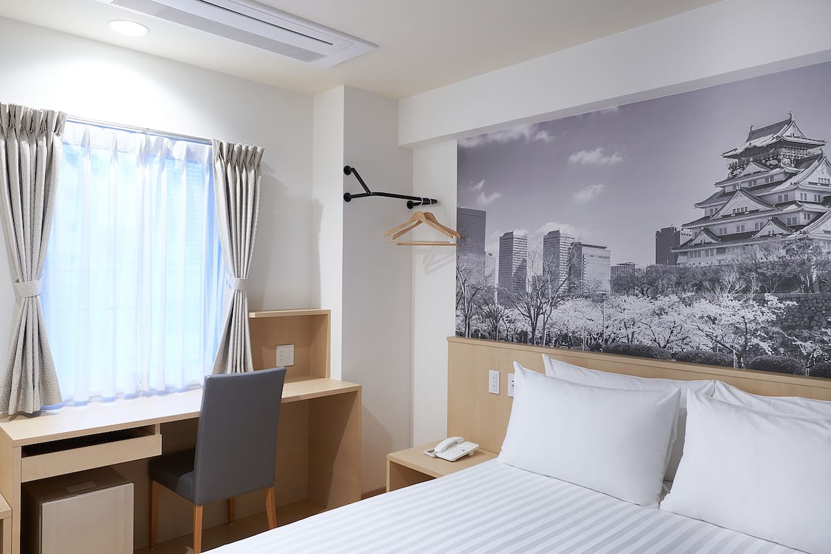 Habitación de hotel con cama, escritorio, silla y un mural urbano en la pared.