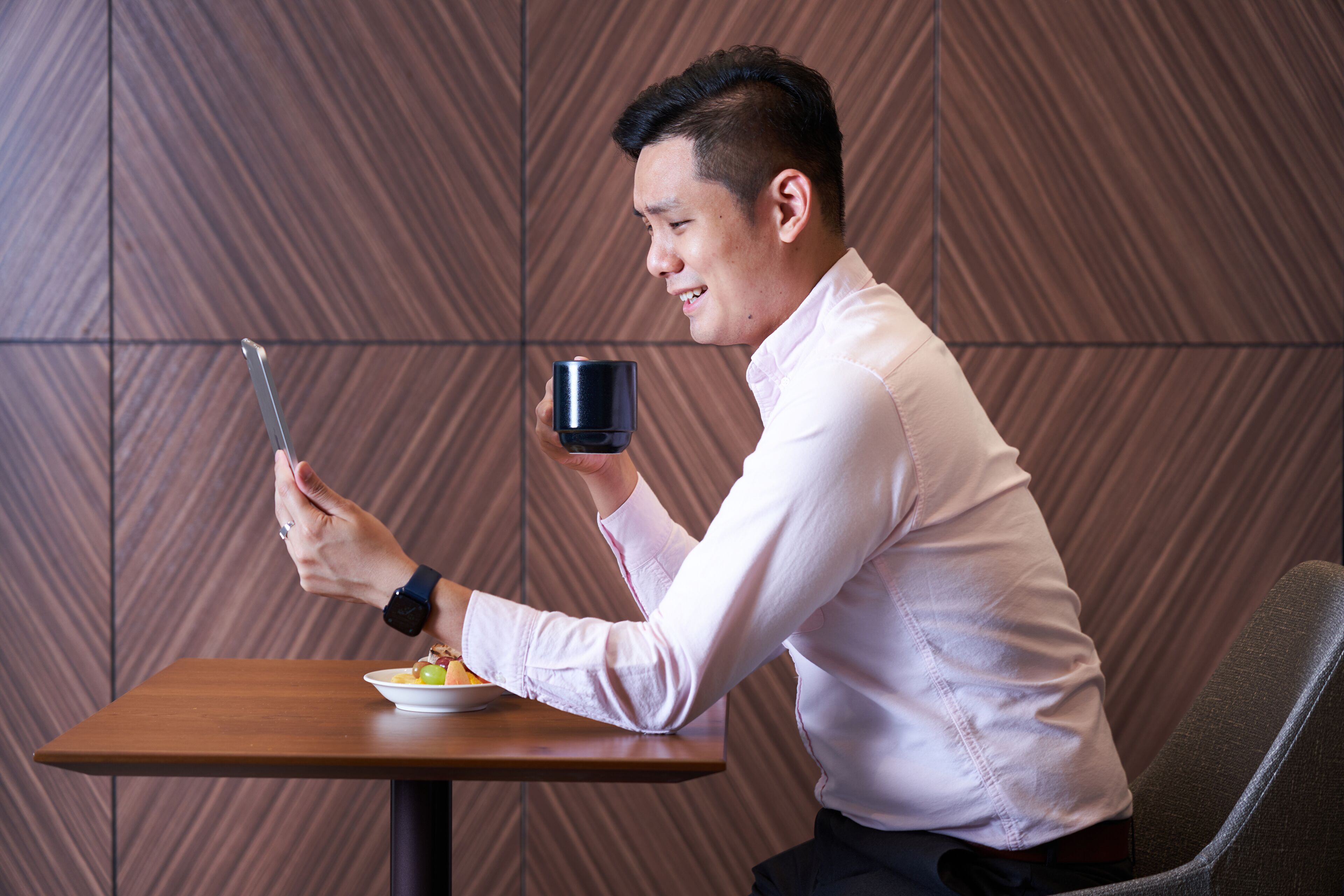 A person seated at a wooden table with a plate of food and a black mug.