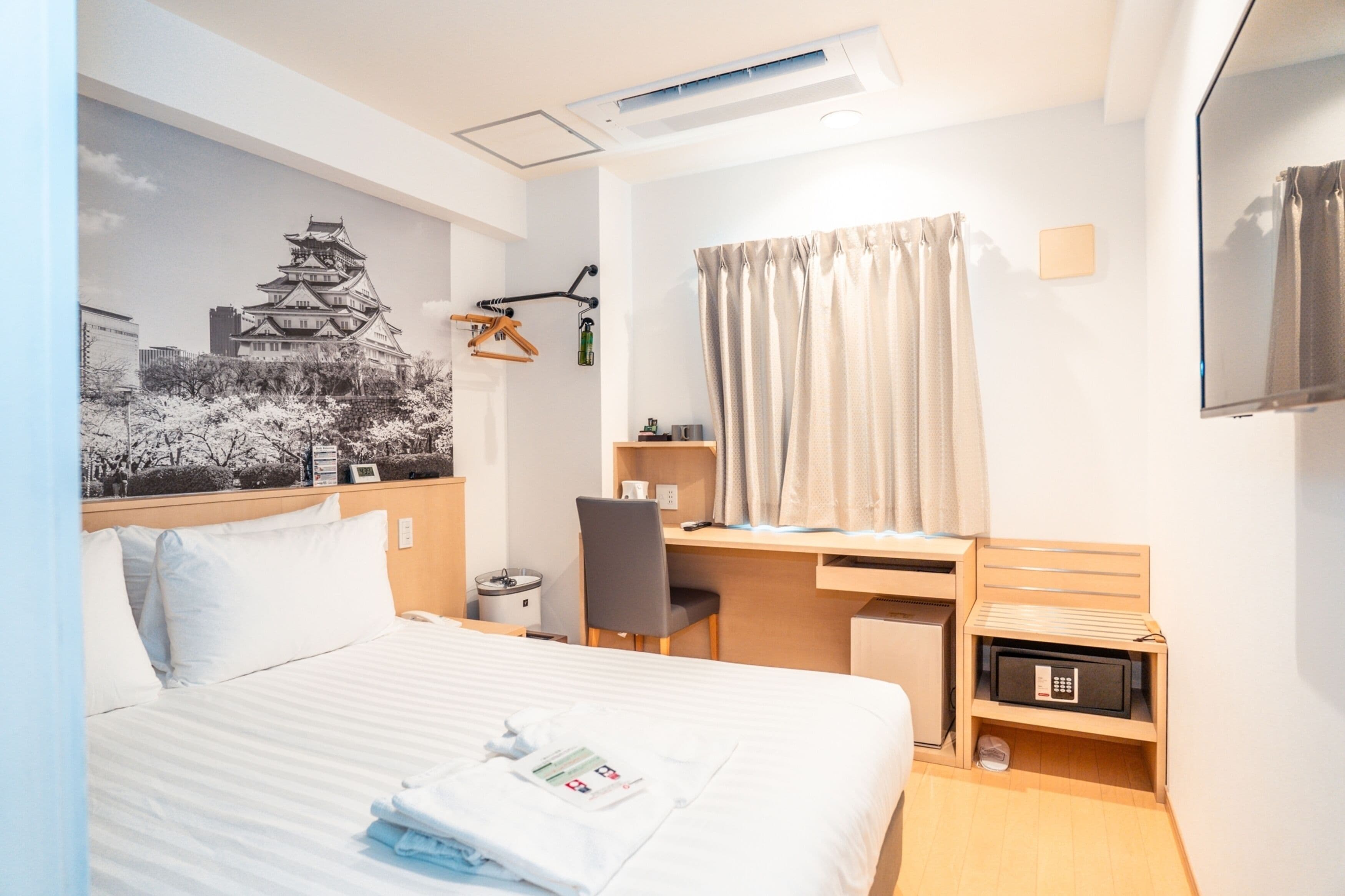 A hotel room with a bed, desk, chair, and a wall-mounted TV.