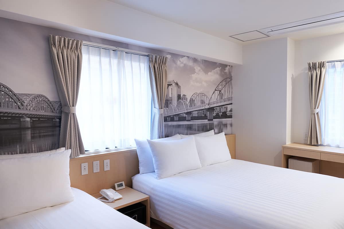 Habitación de hotel con dos camas, una mesita de noche, un teléfono y un mural en la pared de un puente.