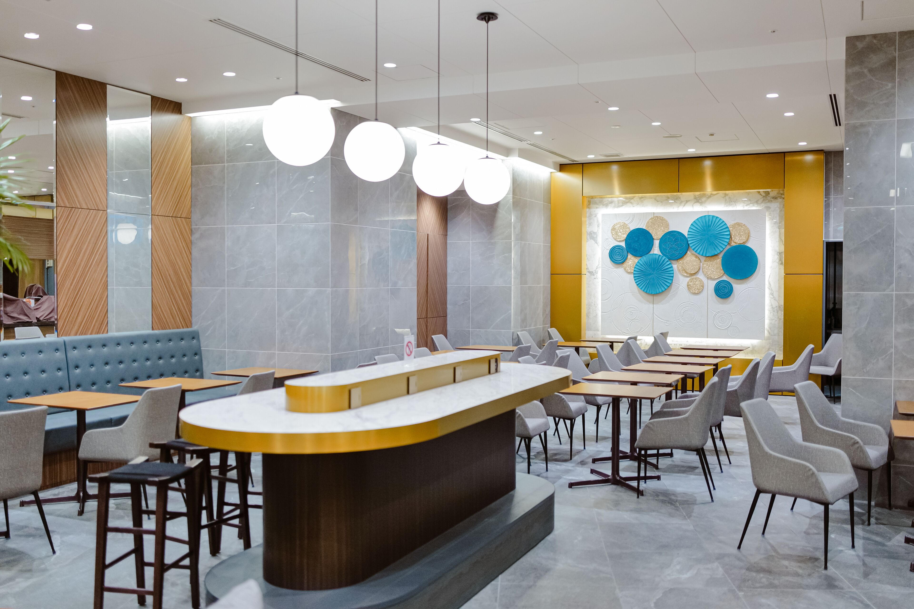 Un restaurant modern amb un taulell central, diverses zones d'aixopluc i una paret decorativa amb motius circulars.