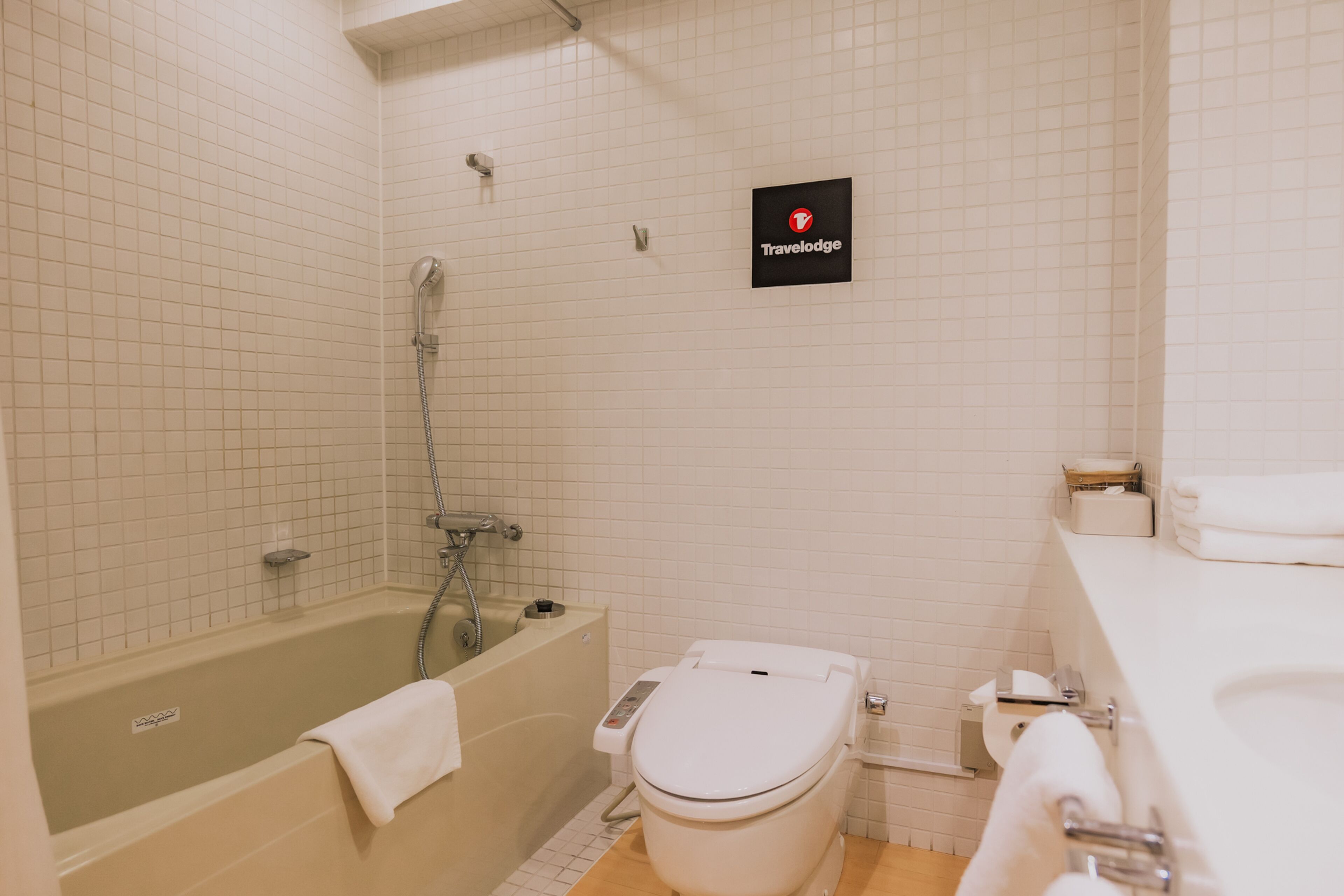 A bathroom with a bathtub, toilet, and a sink. A sign on the wall reads "Travelodge."