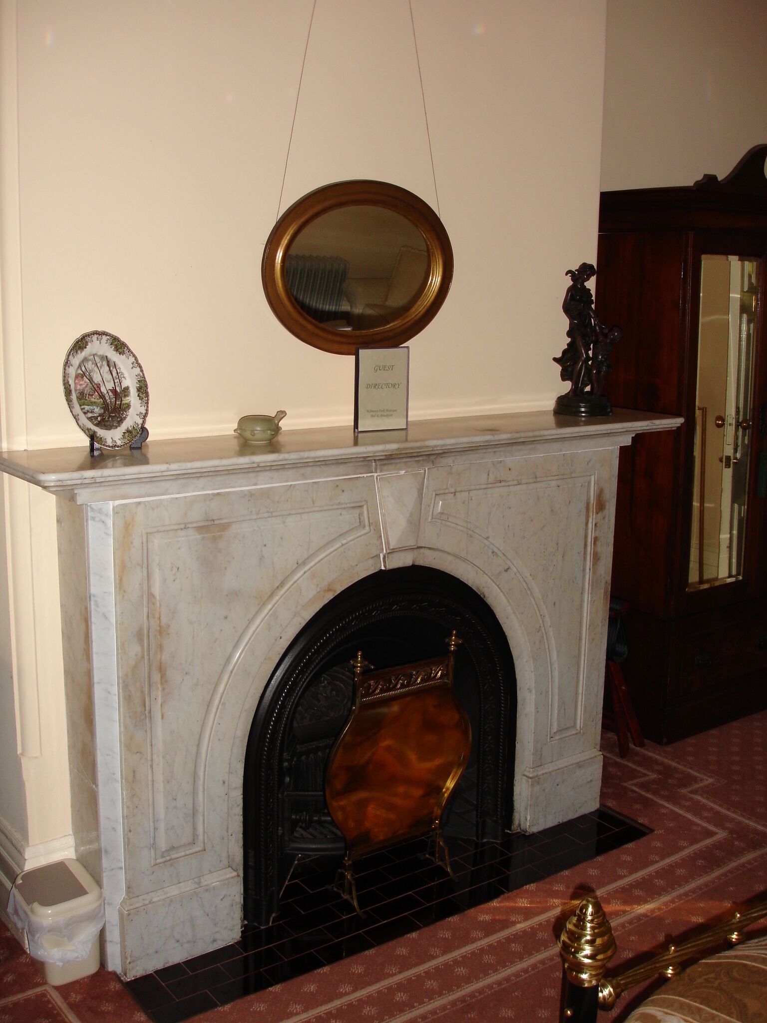 A marble fireplace with a decorative mirror above it, a guest directory sign, and a small plate with a landscape design.