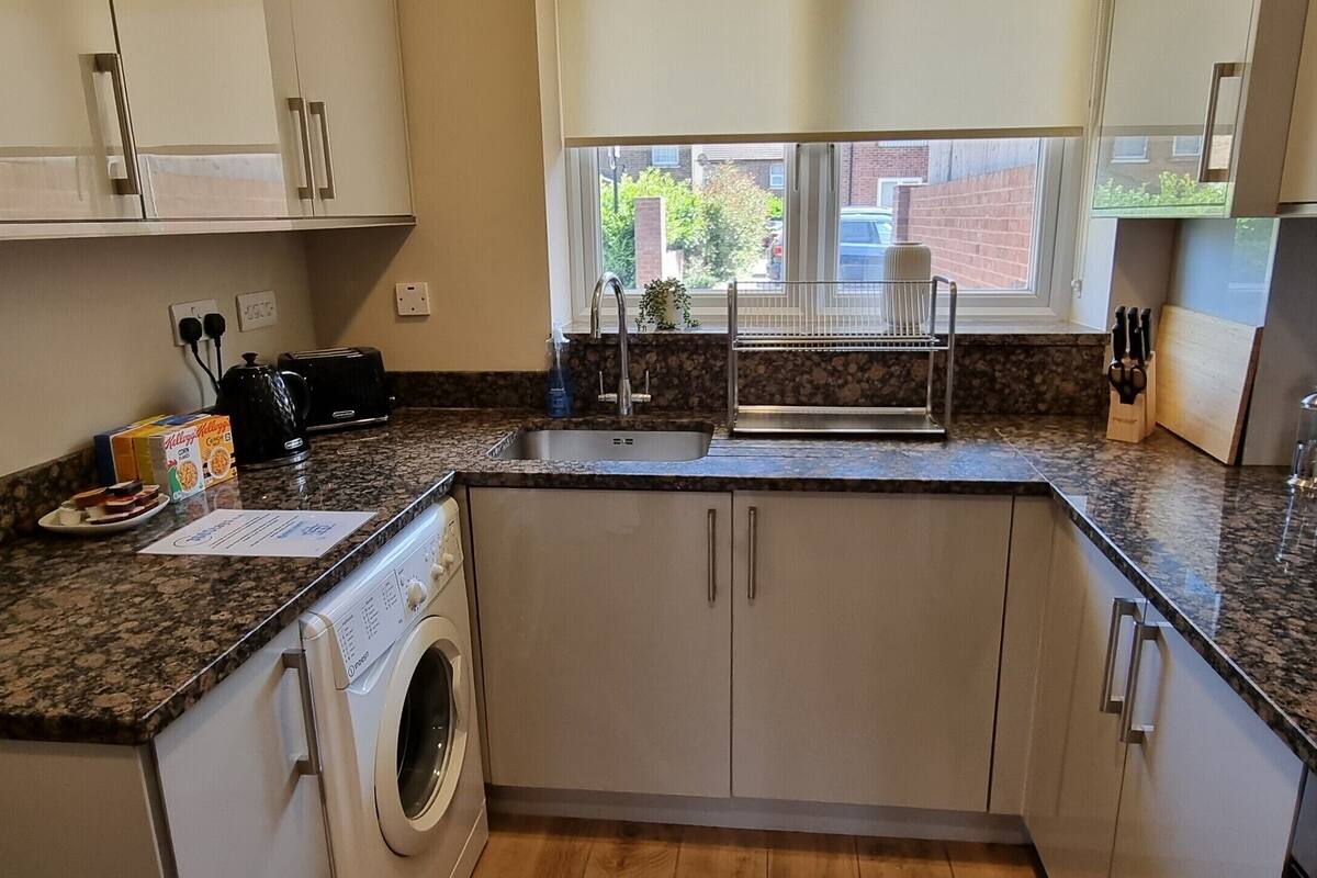 Een kleine keuken met een inbouw wasmachine, een spoelbak en een raam met uitzicht op buiten.
