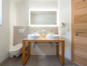 Een badkamer met twee wastafels, een toilet en een houten deur.