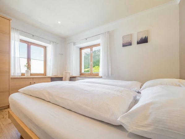 A bedroom with a large bed, two windows, a view of greenery, and a small table with a plant. - In the Center of Neustift - TWO Bedroom Apartment - sleeps 5 (Neustift im Stubaital)