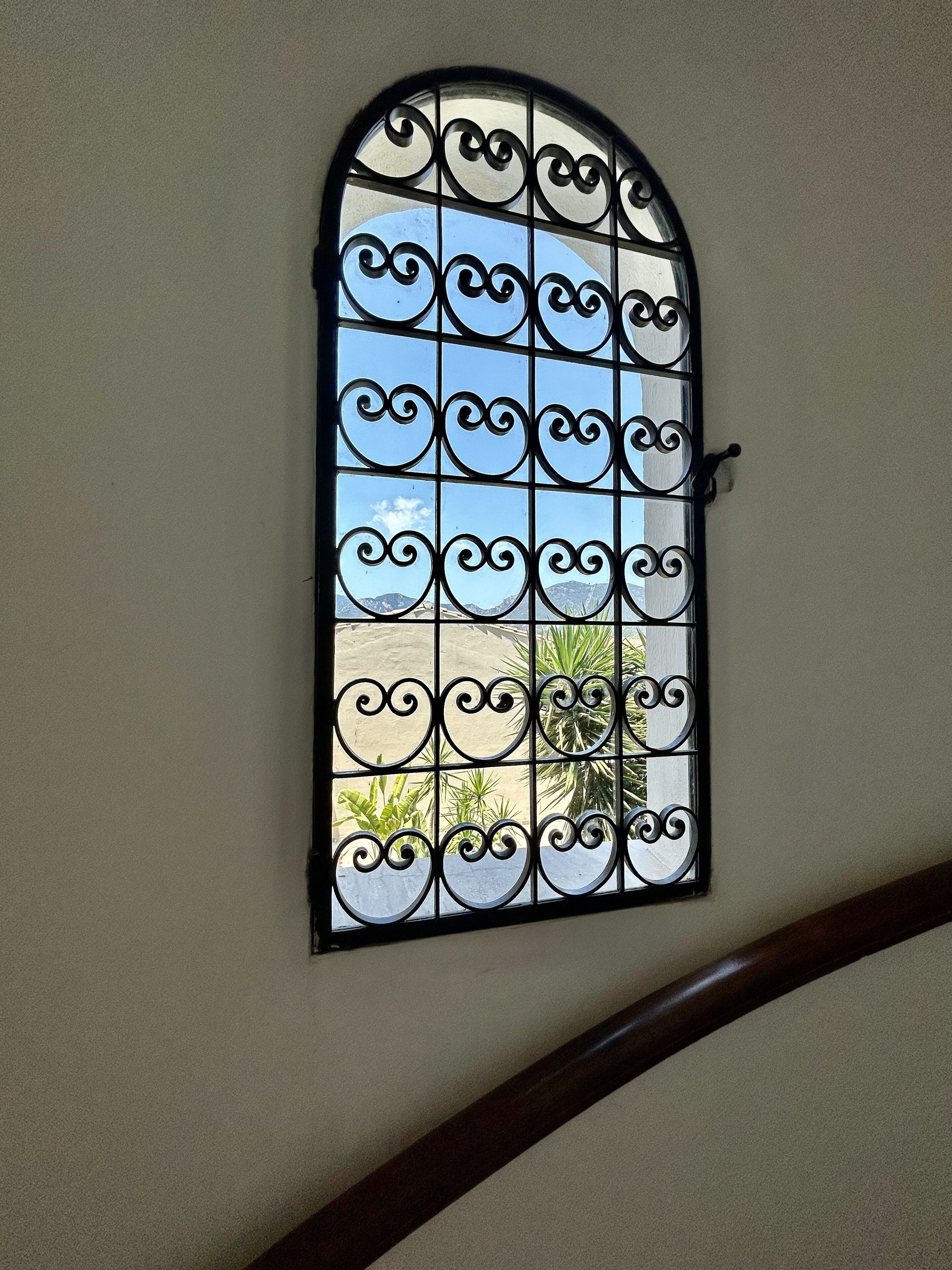 A window with decorative iron bars and a view of a mountain and plants.