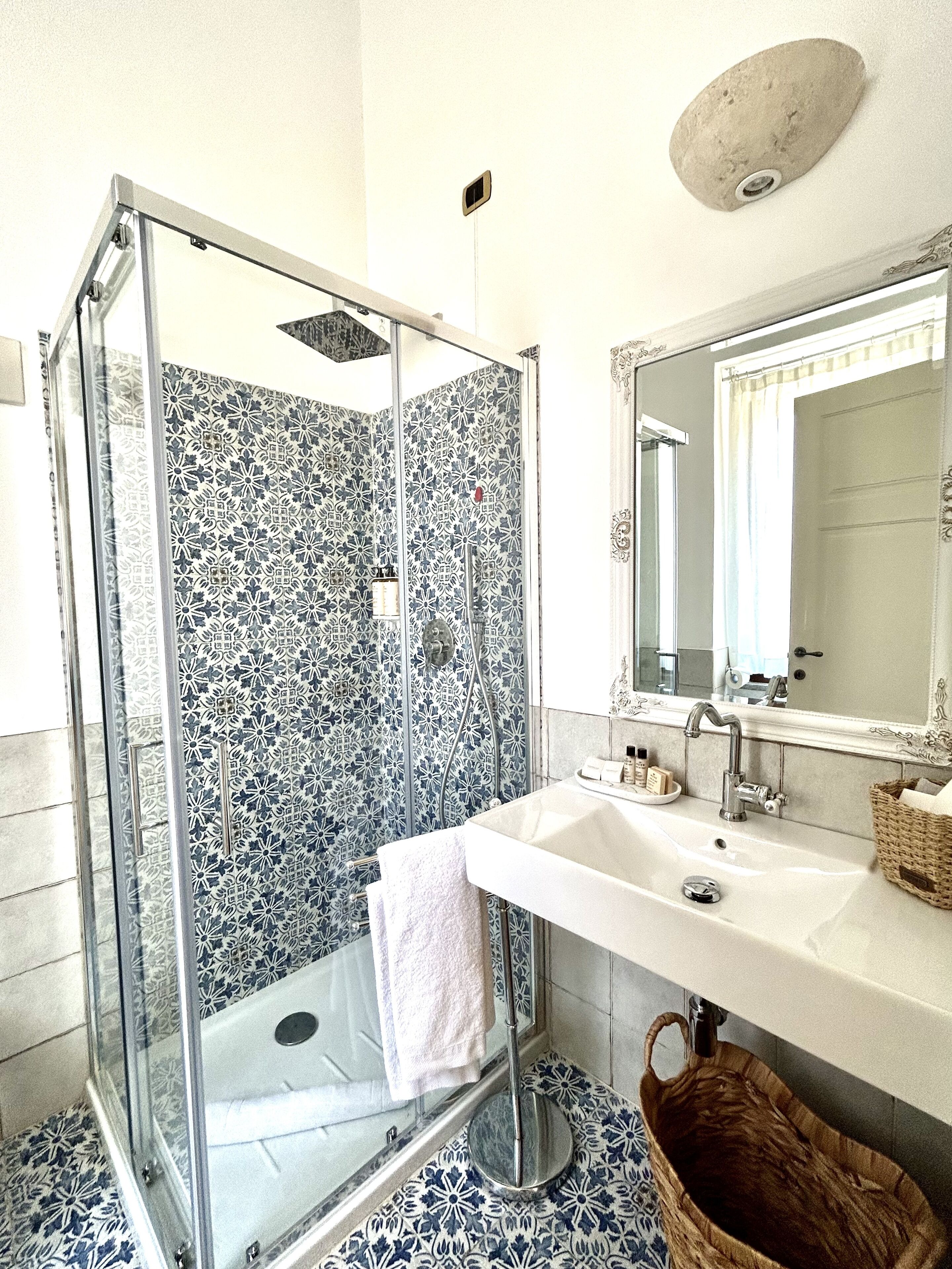 Un baño con ducha acristalada, lavamanos blanco y un espejo grande.