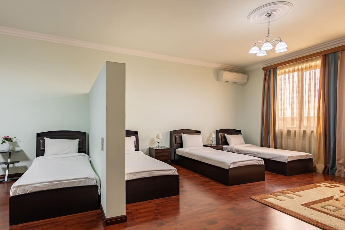 A hotel room with three single beds, a wooden floor, a large window with curtains, and a ceiling light fixture.