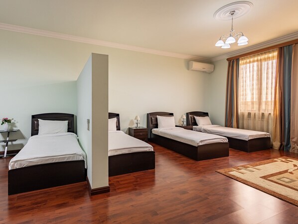A hotel room with three single beds, a wooden floor, a large window with curtains, and a ceiling light fixture. - La Defense Hotel Yerevan (Yerevan)