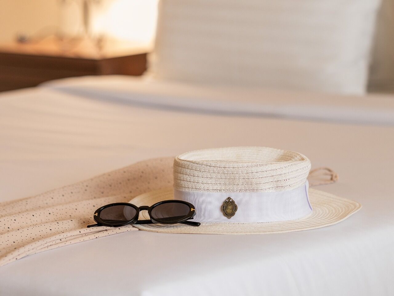 A bed with a white sheet, a straw hat, and a pair of sunglasses.