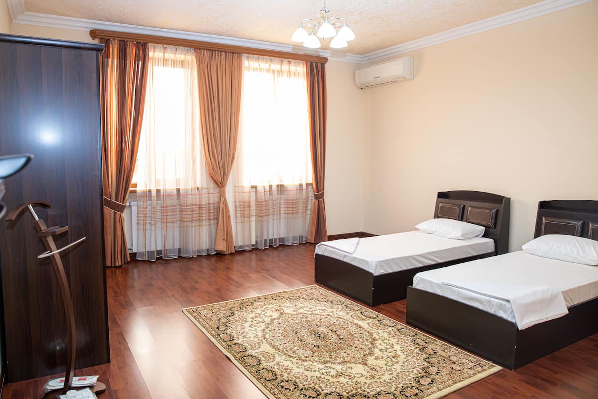 A hotel room with two beds, a wooden floor, a large rug, and a wardrobe.