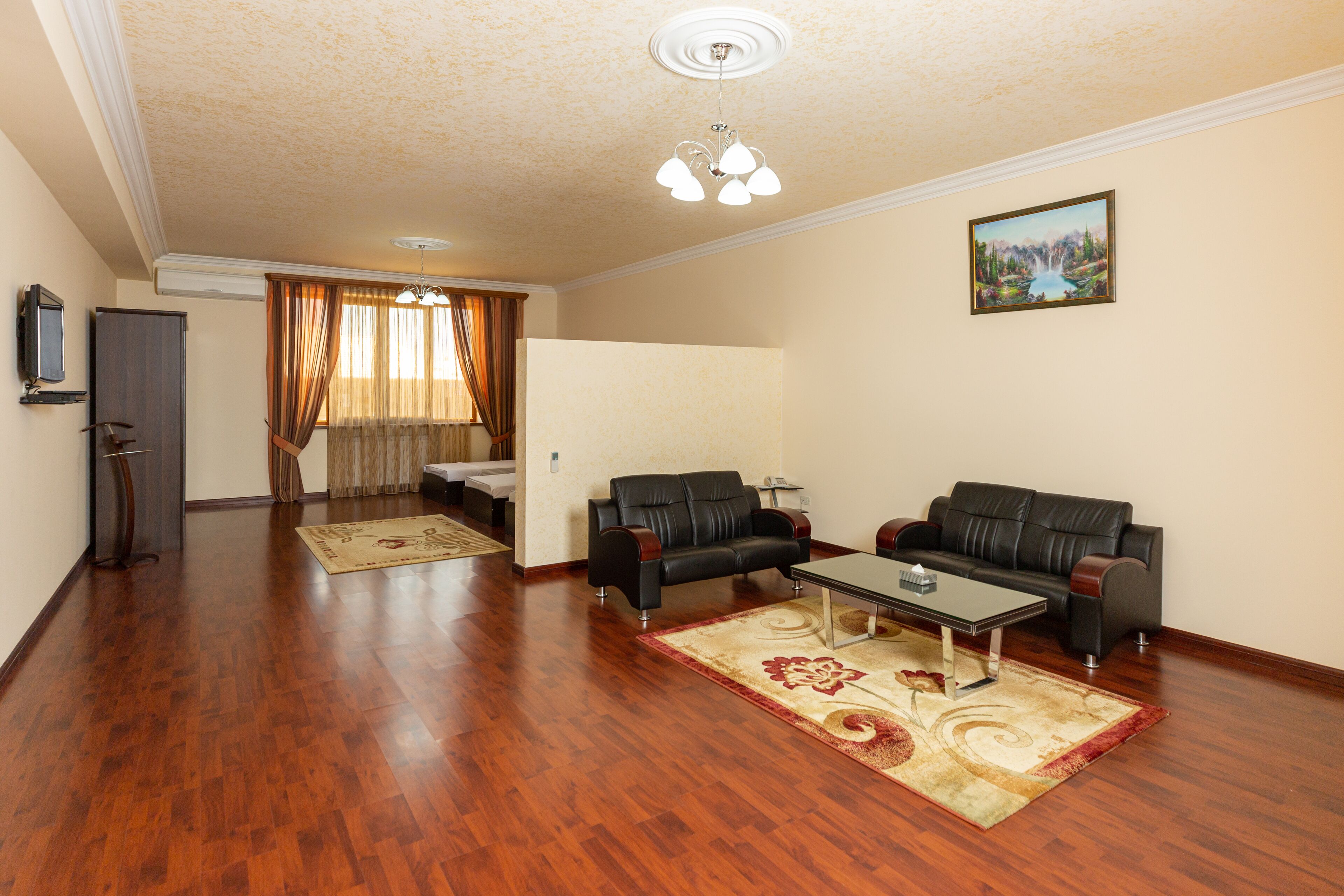 A living room with two black leather sofas, a coffee table, a wooden floor, a ceiling fan, and a painting on the wall.