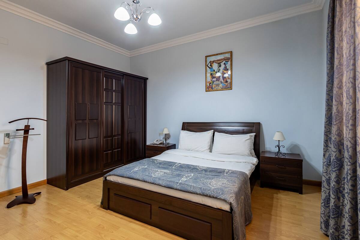 A bedroom with a large bed, wooden wardrobe, and a ceiling light fixture.
