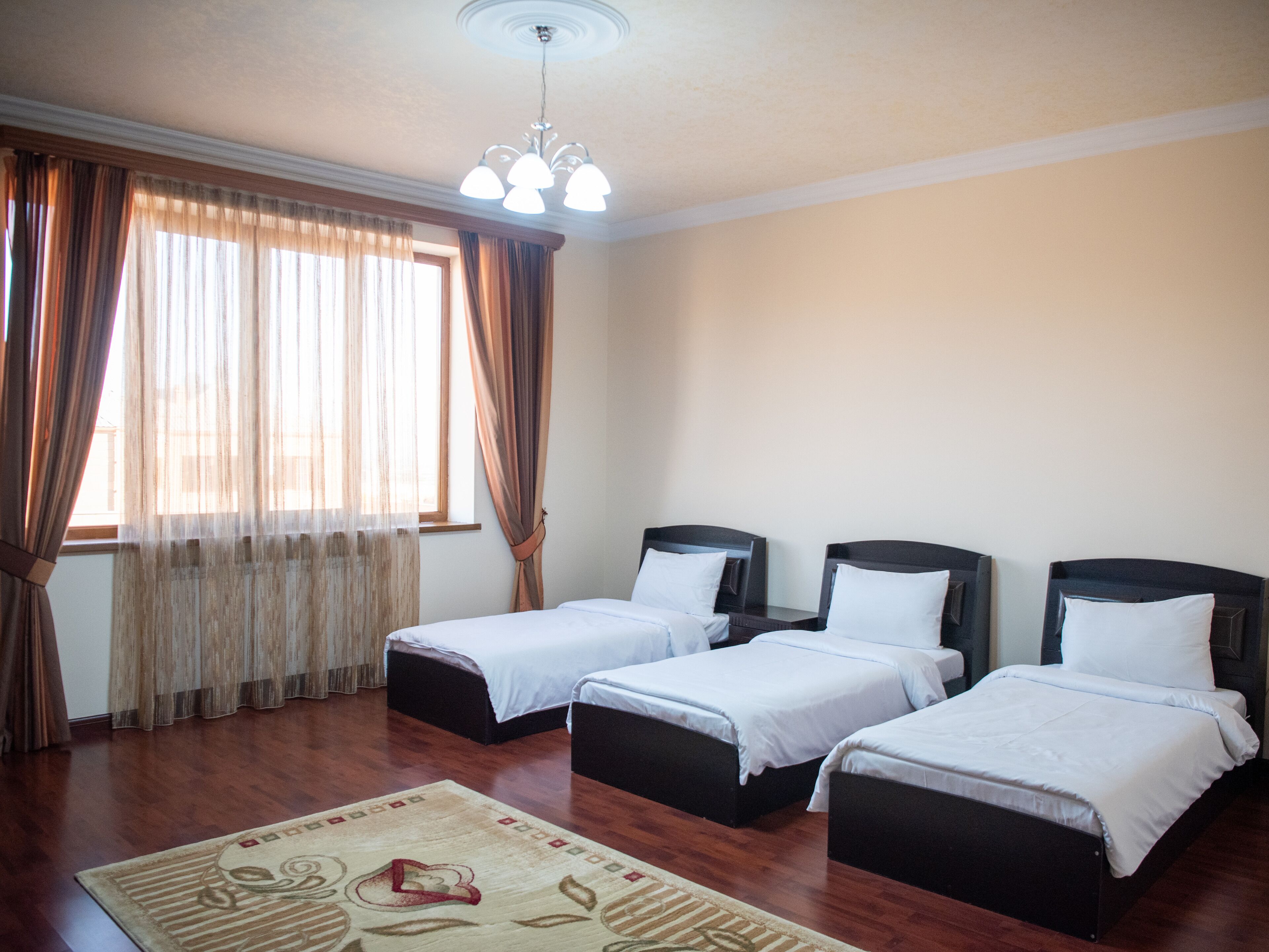 A hotel room with three single beds, a wooden floor, a chandelier, and a window with curtains.