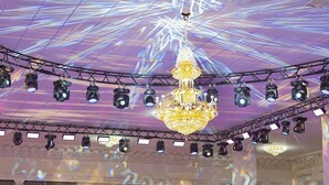 Een balzaal met gedekte tafels voor een formeel evenement, een grote kroonluchter en een plafond met een lichtprojectie.