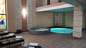 A spa area with a hot tub, lounge chairs, and a pool.