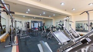 Een fitnessruimte met diverse trainingsapparaten, banken en spiegels.