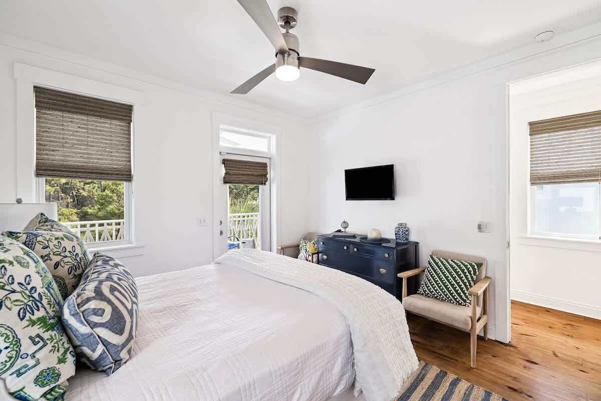 Un dormitorio con cama, ventilador de techo, televisor, cómoda y silla.