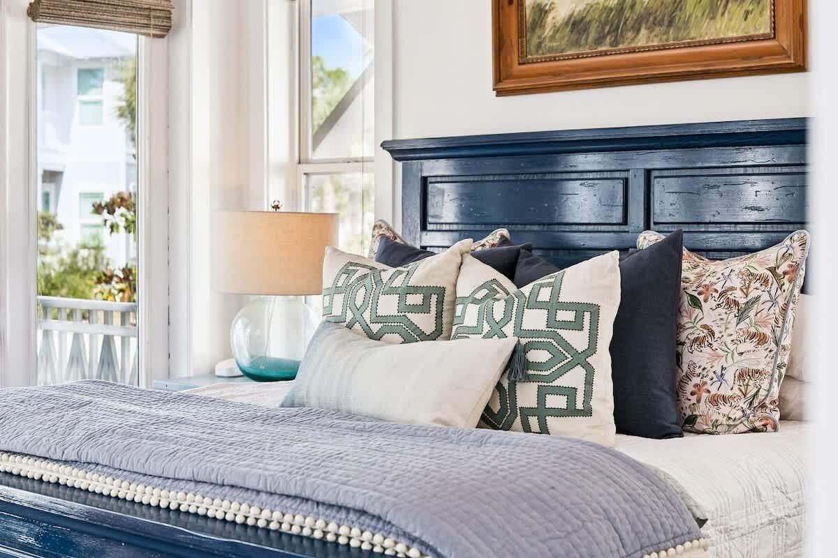 A bed with a dark headboard, multiple pillows, a lamp, and a view of a balcony.